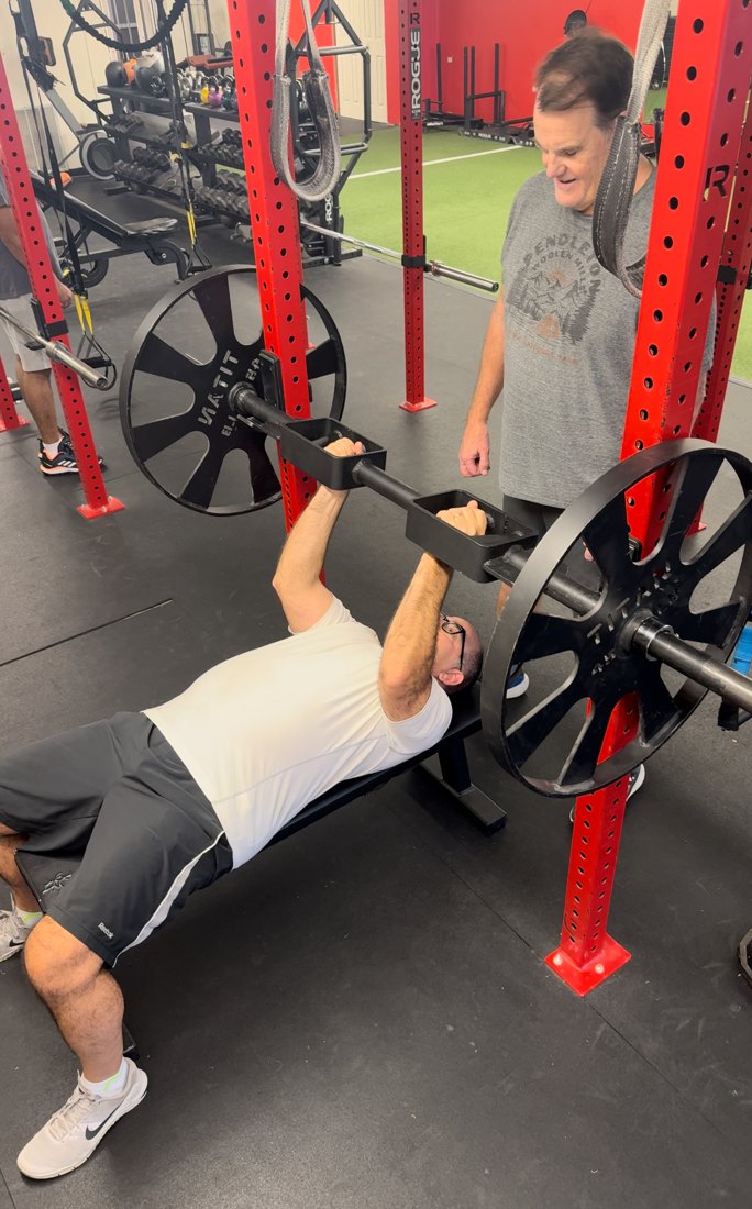 A Ross Fitness member pressing heavy with a coach spotting and cueing every rep